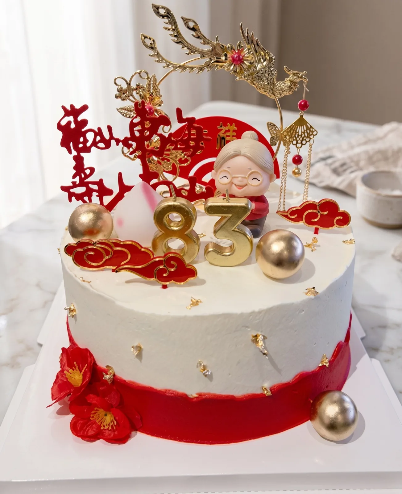 Chinese longevity 83rd birthday cake with gold dragon topper, red cloud accents and grandmother figurine